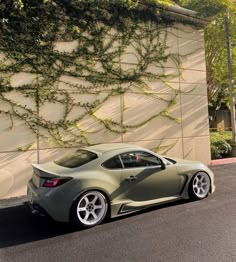 a grey sports car parked in front of a wall with ivy growing on it's side