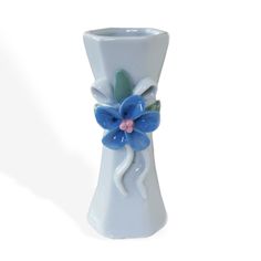 a white vase with a blue flower on the top and green leaves on the bottom