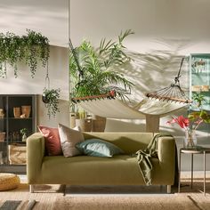 a living room filled with lots of furniture and plants on the wall above it is a hammock