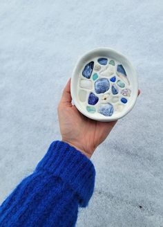 a hand holding a white bowl with sea glass on it in the middle of snow