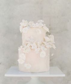 a three tiered cake with white flowers and leaves on the top is sitting on a stand