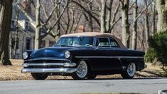 an old black car parked on the side of the road in front of some trees