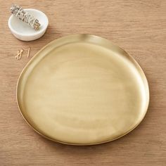 a gold plate next to a small white bowl on a wooden table with scissors and other items