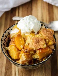 a bowl filled with fruit and ice cream on top of a wooden table next to a spoon