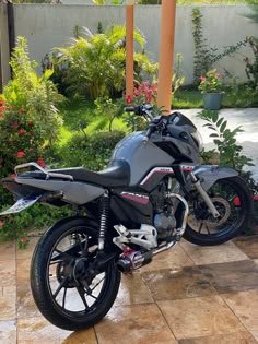 a motorcycle is parked on the sidewalk in front of some bushes and flowers, near a house