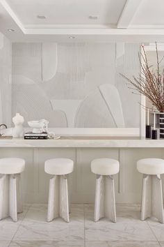 three white stools sit in front of a counter with books and vases on it