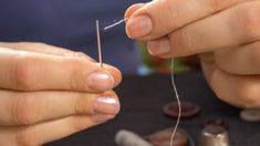 a person is sewing on a piece of thread with their hands and needle in the other hand