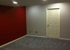 an empty room with red walls, carpet and white door in the middle is shown