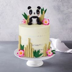 a panda bear sitting on top of a cake with bamboo sticks and flowers around it