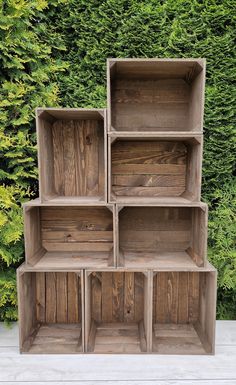 three wooden shelves are stacked on top of each other in front of a green hedge