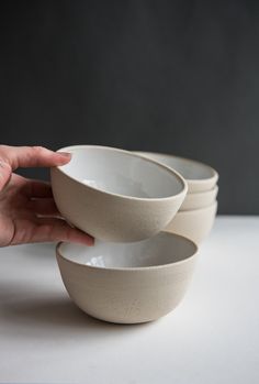 a person holding three white bowls in their hand