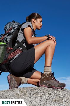 a woman sitting on top of a rock with a backpack