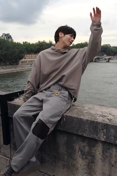 a young man sitting on the edge of a stone wall with his hand in the air