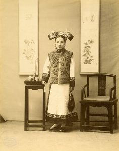 an old black and white photo of a woman standing in front of two wooden chairs