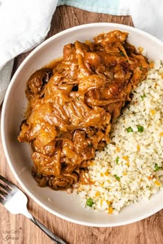 a white bowl filled with rice and meat next to a fork on top of a wooden table