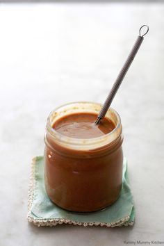 a jar filled with brown liquid sitting on top of a green napkin next to a spoon