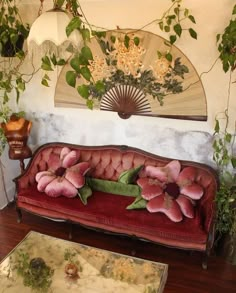 a red couch with pink flowers on it in front of a fan and other decorations