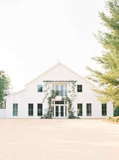 a large white barn with greenery on the front door and windows is featured in this wedding photo