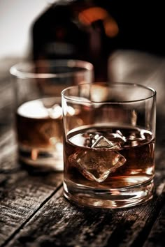 two glasses filled with ice sitting on top of a wooden table