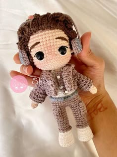 a crocheted doll wearing headphones is being held by someone's hand