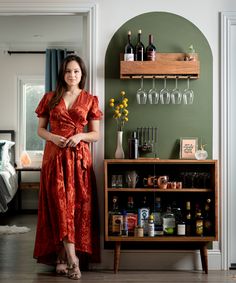 a woman standing in front of a bar with bottles and glasses on the wall behind her