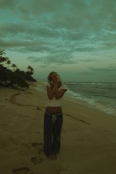 a woman standing on top of a sandy beach next to the ocean while talking on a cell phone