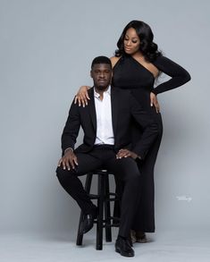 a man and woman sitting on top of a stool posing for the camera with their arms around each other