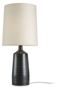 a black table lamp with a white shade on the base and a cord plugged into it