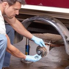 a man working on an air conditioner under a vehicle's hood with gloves