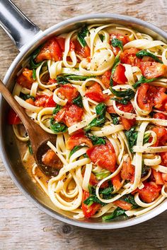 a pan filled with pasta and vegetables on top of a wooden table