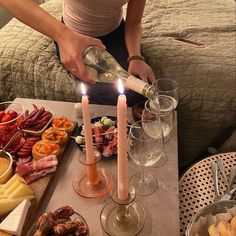 a woman pouring wine into some glasses with food on the table in front of her