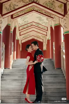 a man and woman are standing on the stairs in front of an ornate building with red pillars