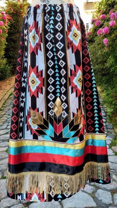 A Tribal Black print ribbon skirt with a multi -colored feather design of black, turquoise, red and gold with gold thread sewn around entire feather design. Gold nylon fringe embellishing the bottom of ribbon work with special multi -colored ribbon above ribbon work. A one channel waistband with a paper bag waist. Ribbon Skirts Native American For Sale, Ribbon Skirts Pattern, Native Dresses, Feather Applique, Native Clothing, Culture Dress, Jingle Dress