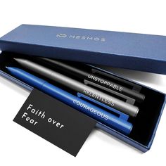 three pens sitting in a blue box on top of a white table next to a card