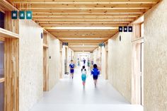 several people walking down a long hallway with wooden walls and ceilinging on both sides