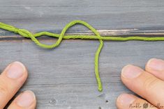 two hands holding a green string on top of a wooden table