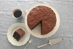 a chocolate cake sitting on top of a white plate next to a cup of coffee