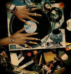 several hands on top of a record player surrounded by assorted jewelry and other items