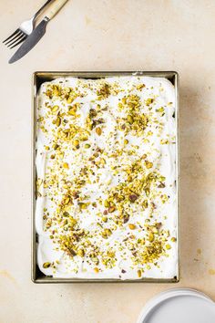 a square pan filled with white frosting and chopped pistachios on top