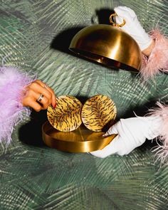 a person in white gloves holding two cookies on top of a gold platter with feathers around it