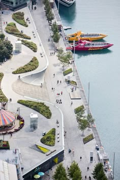 an aerial view of boats docked in the water and people walking on the sidewalk next to them