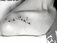 a black and white photo of a woman's shoulder with birds flying around it