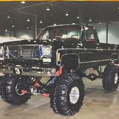 a large black truck with big tires parked in a garage next to other cars and trucks