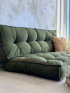 a green couch sitting in front of a window next to a pillow on the floor