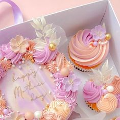 a box filled with cupcakes covered in frosting and pink icing on top of a table