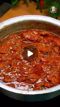 a pot filled with meat and sauce on top of a wooden table next to flowers