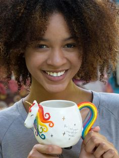 a woman holding a coffee mug with a rainbow unicorn on it's side and smiling at the camera