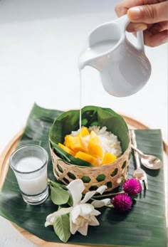 a person pouring milk into a bowl filled with fruit and vegetables on top of a banana leaf