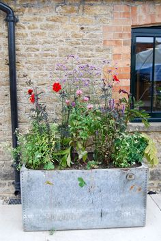 a metal planter filled with lots of flowers next to a brick wall and window