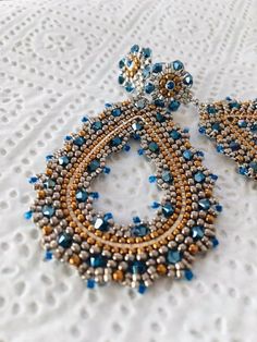 a pair of blue and gold beaded earrings on top of a white tablecloth